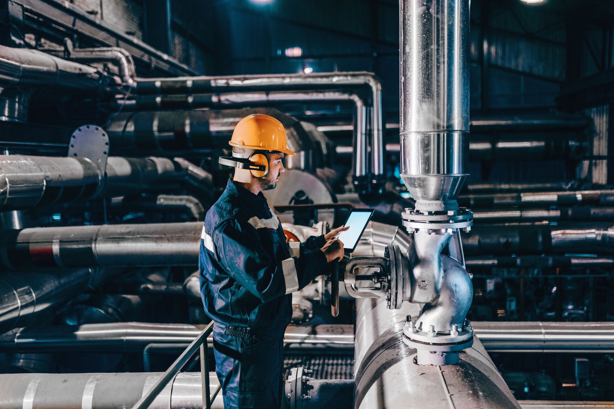 Portrait of young Caucasian man dressed in work wear using tablet while standing in heating plant.